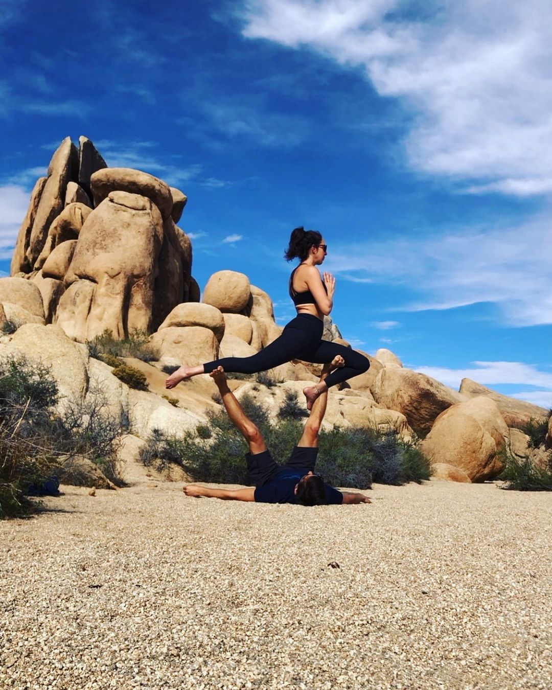 Aly flying a warrior pose on Steve in Joshua Tree National Park